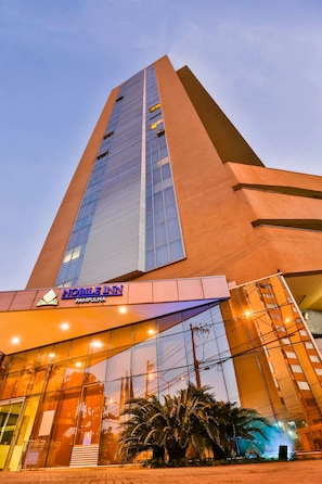 Un edificio alto de diseño moderno, con una entrada destacada que cuenta con puertas de vidrio y un letrero que dice "NOBLE INN PAMPULHA".