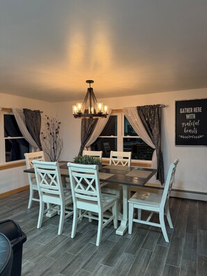 A dining area with a chandelier, white chairs, a dark wooden table, and a wall sign.