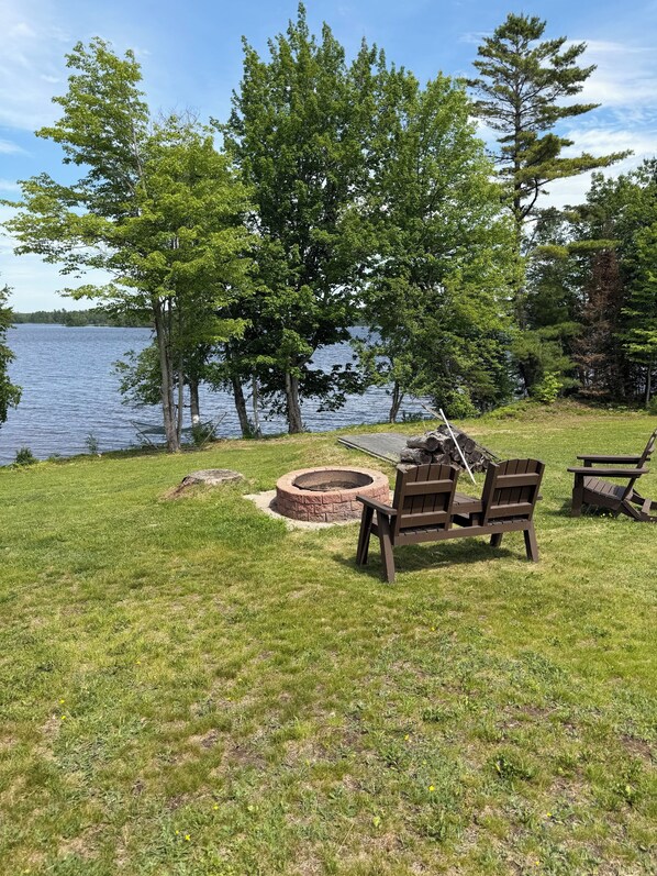 A lakeside outdoor seating area with a fire pit and Adirondack chairs.