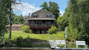 A two-story house with a balcony, a dock, and a grassy area. - Waterfront lake house retreat located in Baileyville Maine! (Baileyville)