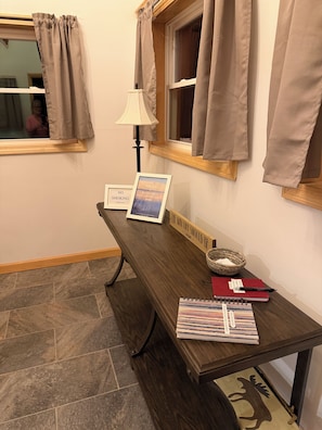 A wooden bench with a lamp, a framed welcome sign, a no smoking sign, a red notebook, and a spiral-bound planner.