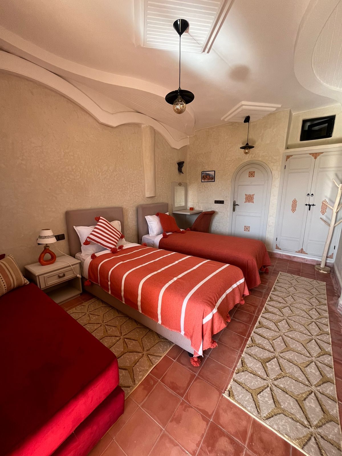 A bedroom with two beds, a nightstand, a lamp, a wardrobe, and a ceiling fan.