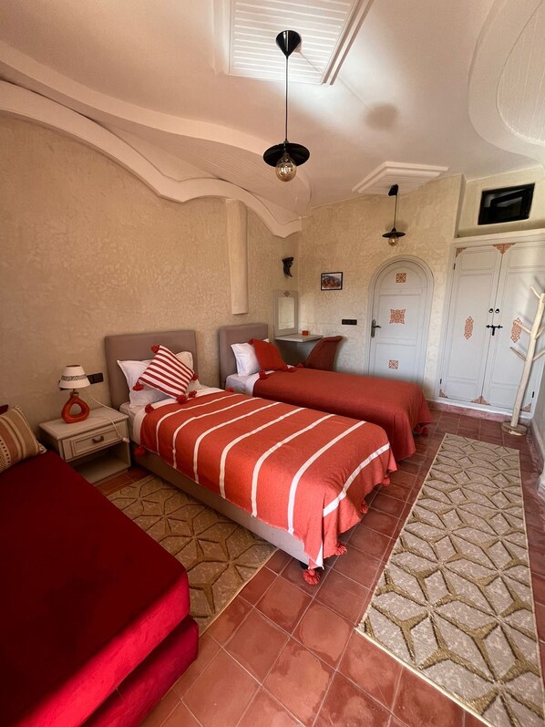A bedroom with two beds, a nightstand, a lamp, a wardrobe, and a ceiling fan.