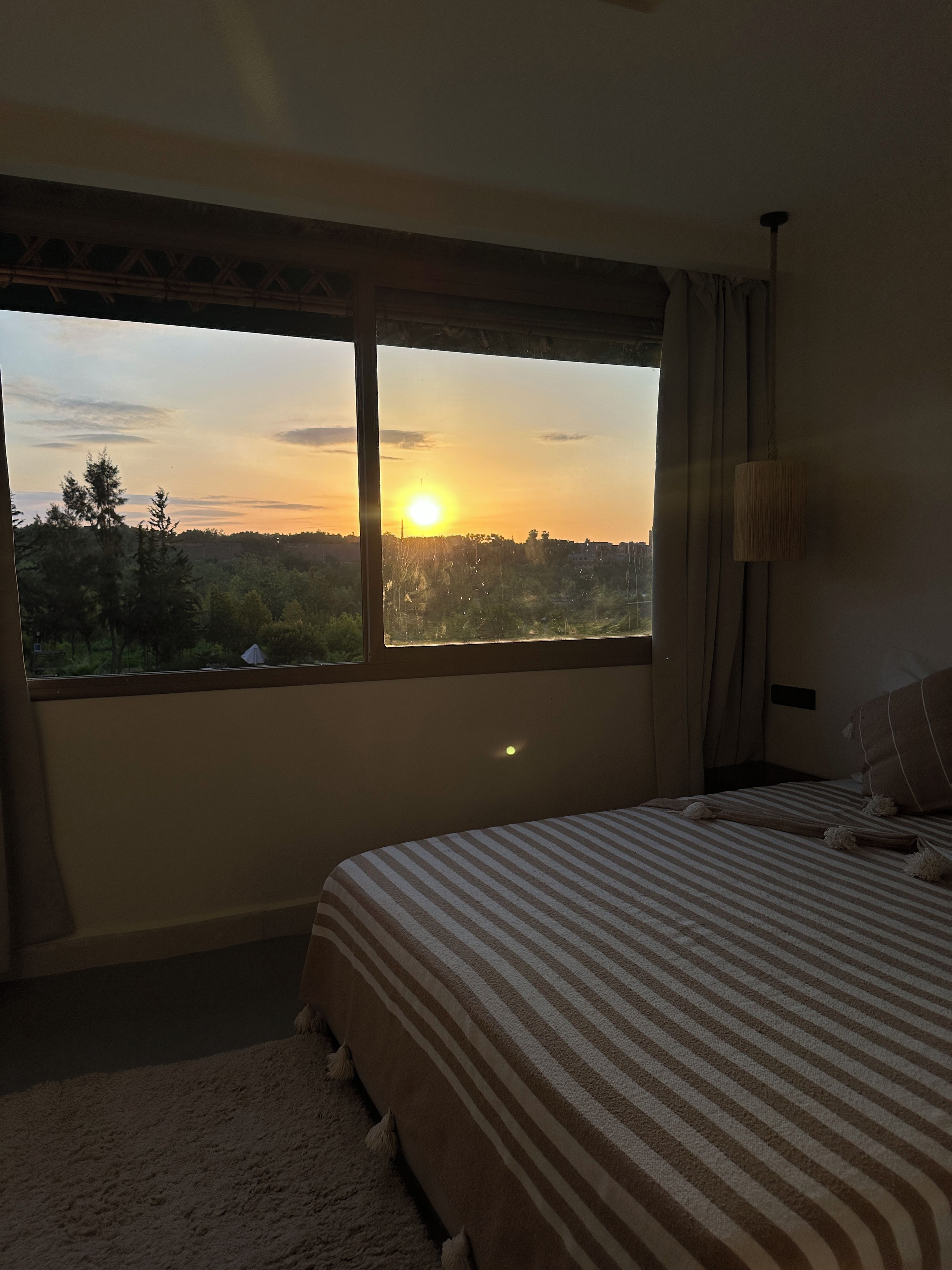 A bedroom with a large window, a bed with striped bedding, and a view of a landscape.
