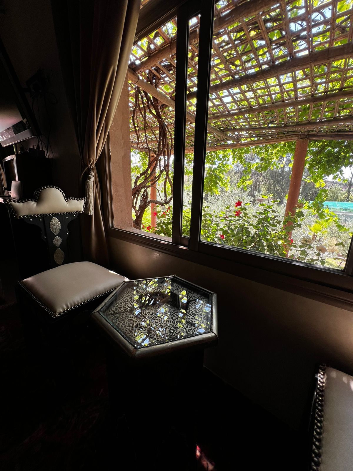 A room with a view of a garden through a window with a wooden trellis.