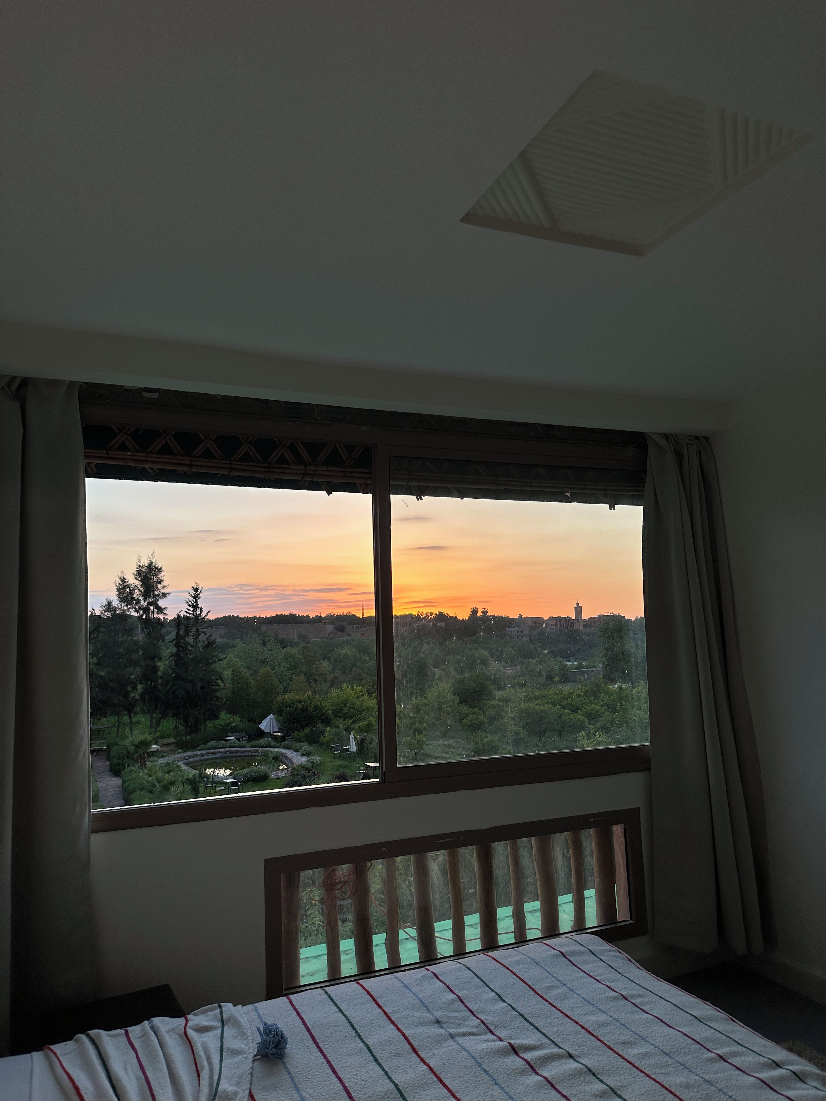 A room with a large window overlooking a garden and a sunset view.