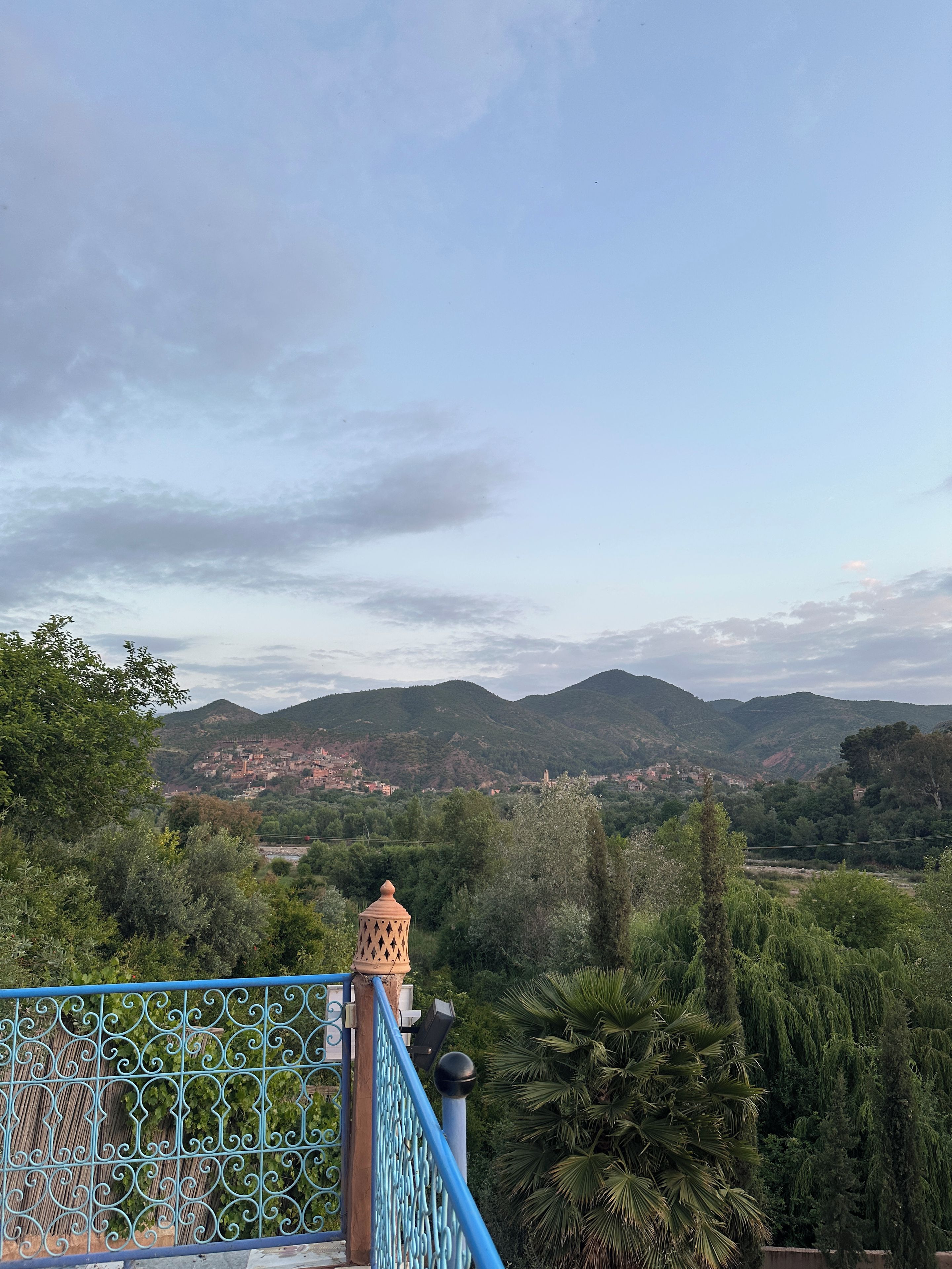 A view of a mountainous landscape with a town in the distance, a blue railing, and lush greenery.