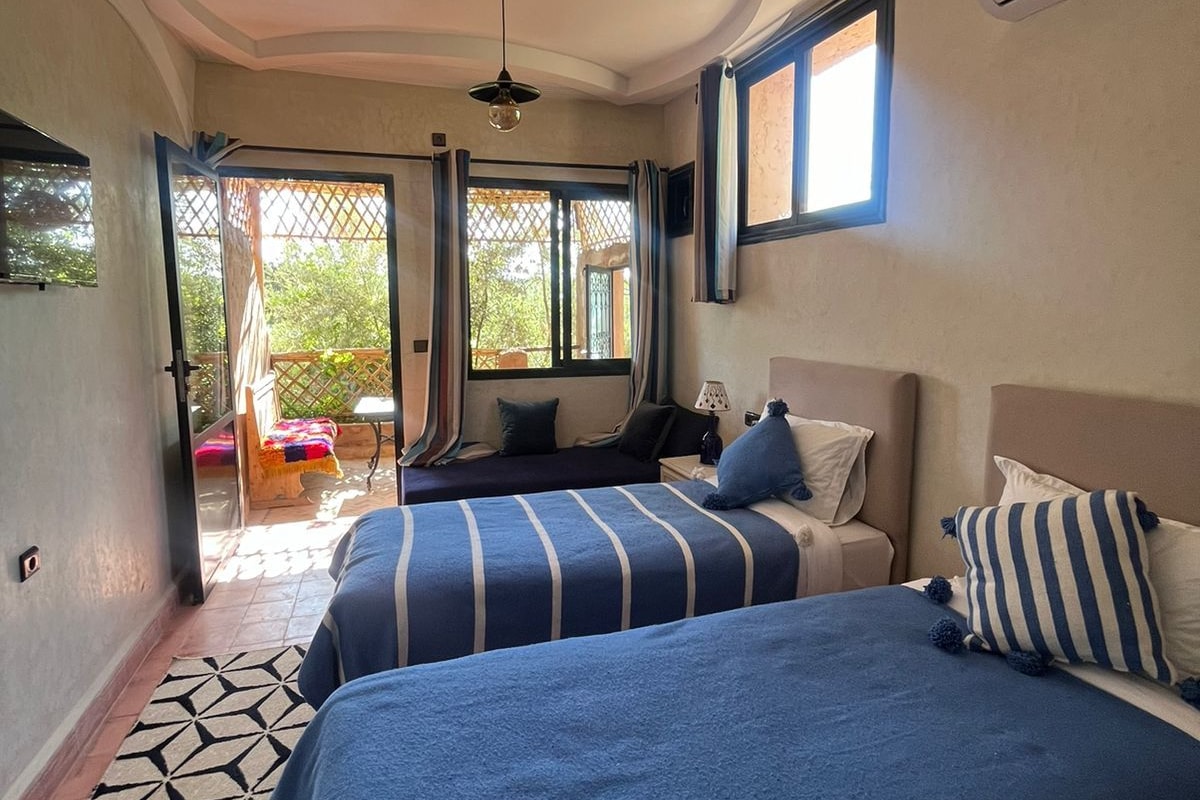 Un dormitorio con dos camas, una alfombra estampada, un ventilador de techo y vistas a un espacio exterior.