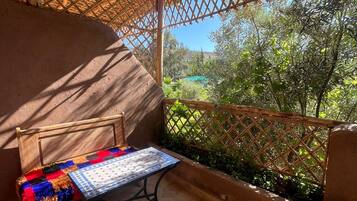 A balcony with a woven trellis, a bench with a colorful cushion, and a view of greenery.