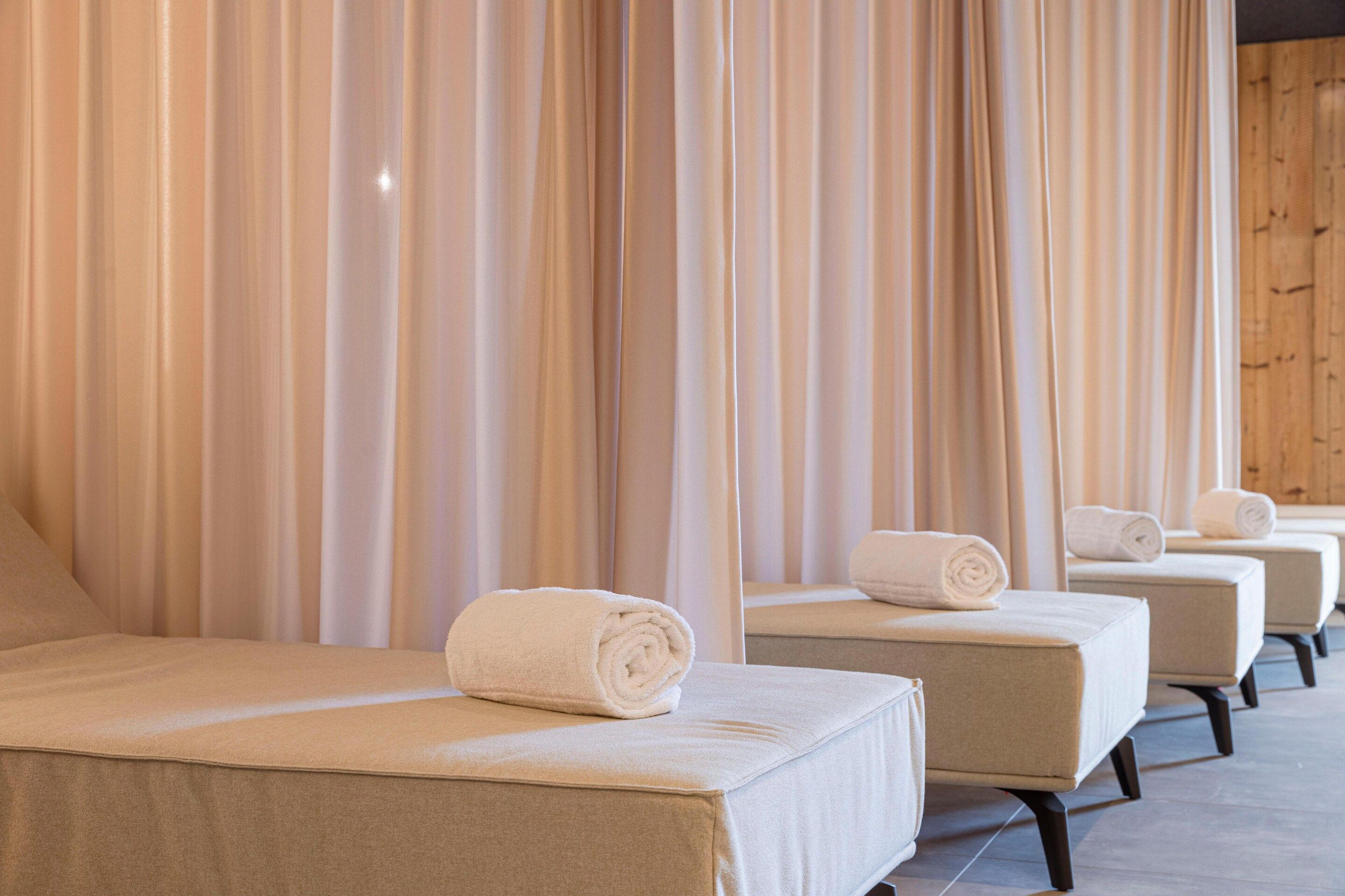 A row of neatly arranged beds with towels, a wooden wall, and a curtain backdrop.
