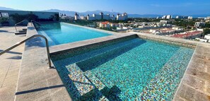 Piscina com piso em mosaico e vista para o horizonte da cidade.