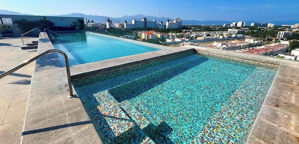 A swimming pool with mosaic tile flooring and a view of a cityscape in the background. - Brand New Condo Brisa Nayar 204 - Rooftop Pool & Ocean Views (Las Jarretaderas)