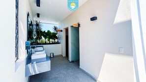 A narrow hallway with a kitchenette area on the left, a door on the right, and a sign indicating 'MUJERES' (women's) and 'HOMBRES' (men's) facilities. - Brand New Condo Brisa Nayar 204 - Rooftop Pool & Ocean Views (Las Jarretaderas)