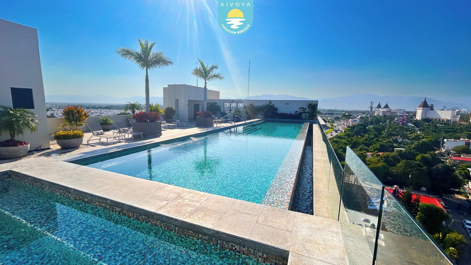 Une piscine sur le toit, avec une eau d’un bleu cristallin, entourée de chaises longues et de plantes en pot.