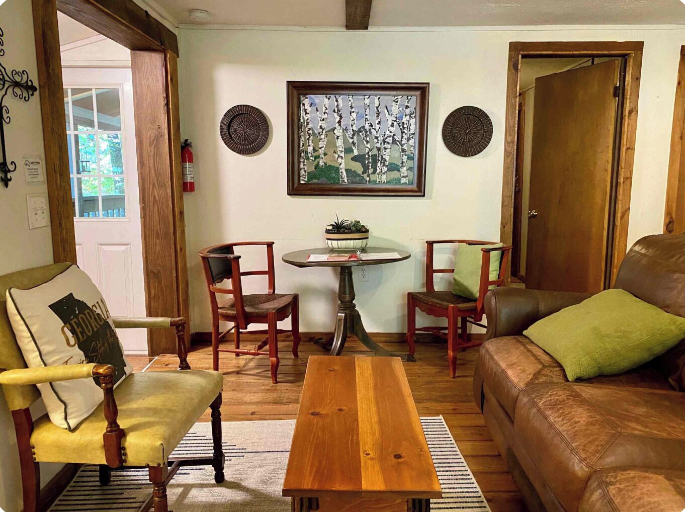 A cozy living room with a wooden coffee table, two wooden chairs, a leather sofa, and a framed picture on the wall.