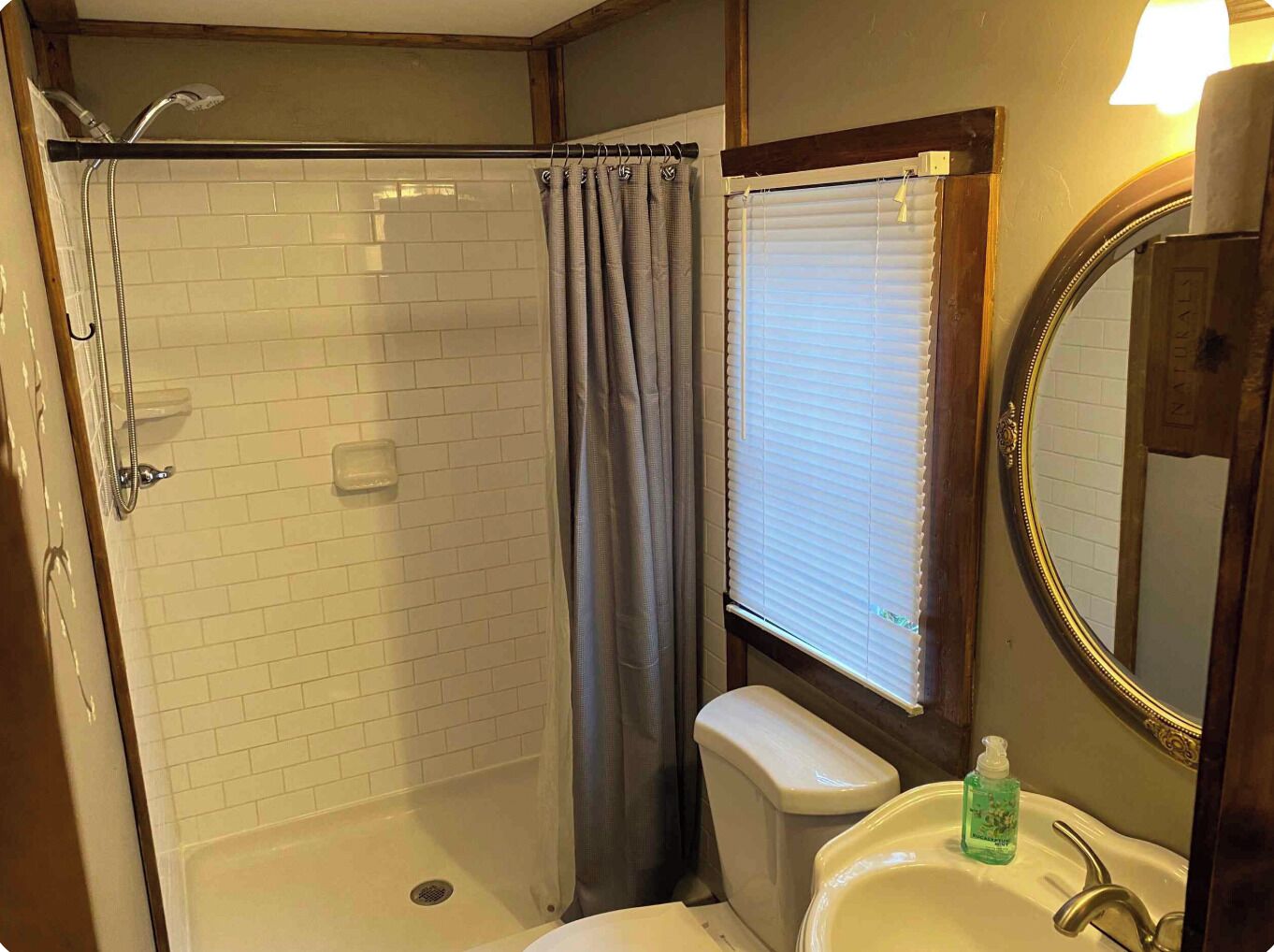 A bathroom with a shower, toilet, sink, and a window with blinds.