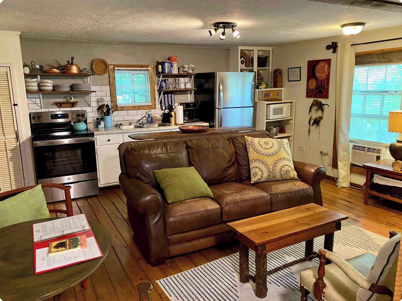 A compact living space with a kitchenette, a brown leather sofa, a wooden coffee table, and a dining area with a chair.