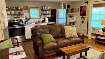A compact living space with a kitchenette, a brown leather sofa, a wooden coffee table, and a dining area with a chair.