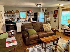Un espacio habitable compacto con kitchenette, un sofá de cuero marrón, una mesa de centro de madera y un comedor con una silla.