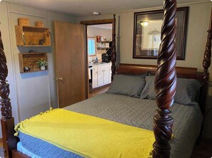 Un dormitorio con cama con dosel, una puerta de madera y una cocina al fondo.