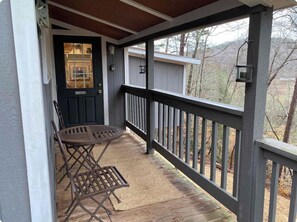 A covered porch with a table and chairs, a door with a 'No Smoking' sign, and a view of trees and hills.