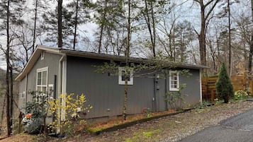 A small, single-story cabin with a sloped roof, surrounded by a wooded area.