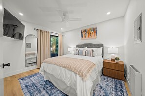 A modern bedroom with a bed, bedside tables, a ceiling fan, a window with curtains, and a wall-mounted artwork. - Steps to Sail Bay · Full 2026 Remodel · Garage Parking · Spa (San Diego)