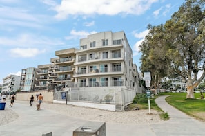 A multi-story residential building with balconies, a sandy ground area, and a pedestrian pathway. - Steps to Sail Bay · Full 2026 Remodel · Garage Parking · Spa (San Diego)