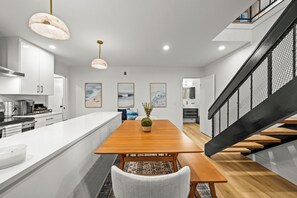 A modern kitchen with white cabinetry, a wooden dining table, and a staircase with a black railing. - Steps to Sail Bay · Full 2026 Remodel · Garage Parking · Spa (San Diego)