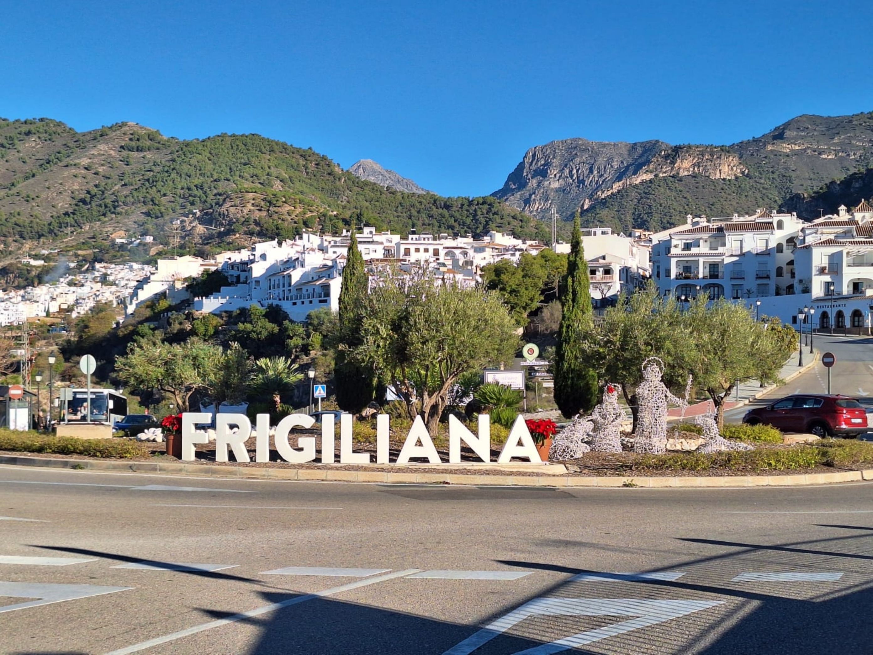 A sign with 'FRIGILANA' indicating a location, with a road in the foreground and a town in the background.