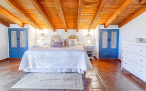 A bedroom with a wooden ceiling, a bed with white bedding, two nightstands, a dresser, and a blue door. - Zambra: 3-Bedroom Villa with Private Pool in Frigiliana (Frigiliana)