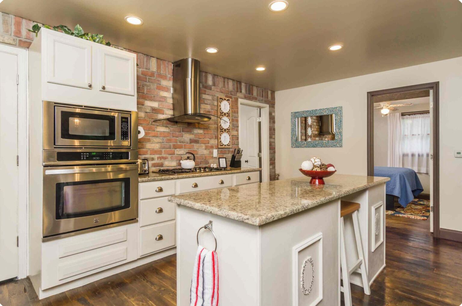 A kitchen with stainless steel appliances, a brick accent wall, and a small island with stools.