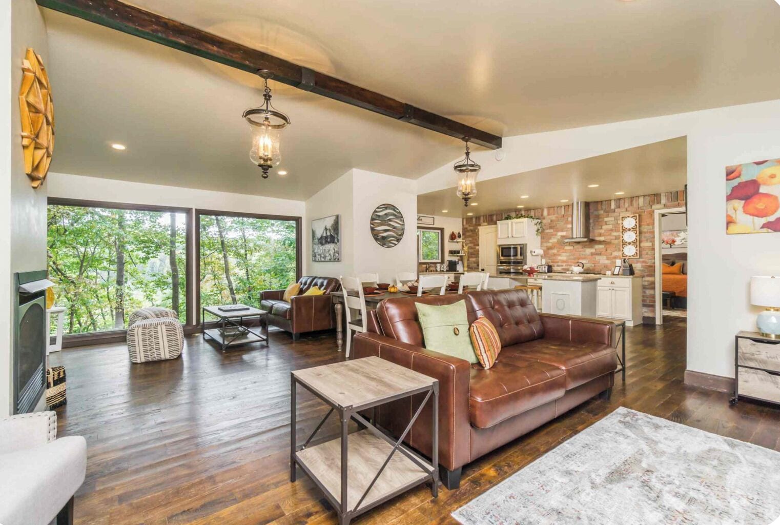 A spacious living room with a leather sofa, a coffee table, and a view of the outdoors through large windows.