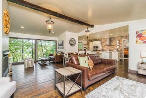 A spacious living room with a leather sofa, a coffee table, and a view of the outdoors through large windows.
