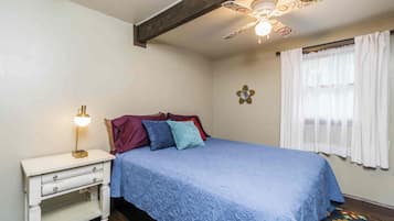 Une chambre à coucher avec un lit, une table de chevet avec une lampe, un ventilateur de plafond et une fenêtre avec des rideaux.