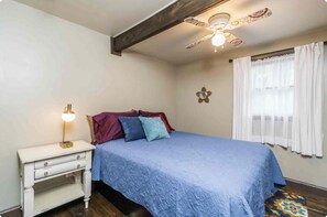 A bedroom with a bed, a bedside table with a lamp, a ceiling fan, and a window with curtains. - Tranquil 2-bedroom cabin in the Woods. 4 mins to charming Dahlonega townsqaure (Dahlonega)