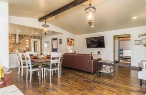 A spacious living area with a dining table, chairs, a brown leather sofa, and a television mounted on the wall. - Tranquil 2-bedroom cabin in the Woods. 4 mins to charming Dahlonega townsqaure (Dahlonega)
