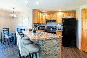 A modern kitchen with wooden cabinets, a black refrigerator, a granite countertop, and a dining area with bar stools. - Perfect Fall Getaway: charming 1-bedroom townhome in Galena on golf course (Galena)