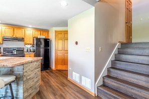 A kitchen with wooden cabinets, a black refrigerator, and a built-in island with a bar stool. - Perfect Fall Getaway: charming 1-bedroom townhome in Galena on golf course (Galena)