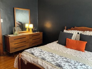 A bedroom with a wooden dresser, a bed with multiple pillows, and a nightstand with a lamp and clock.