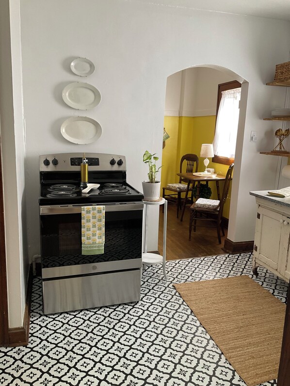 A kitchen with a stove, a dining table with chairs, a potted plant, and a patterned floor.