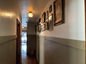 A hallway with framed pictures on the wall, a wooden floor, and a light fixture on the ceiling.