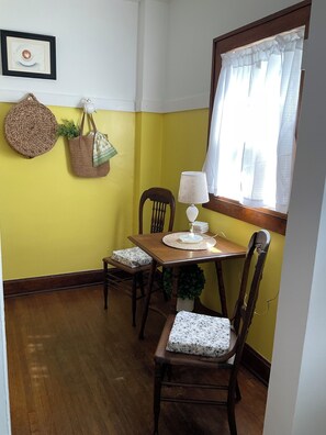 A dining area with a wooden table, two chairs, a lamp, and a window with curtains.