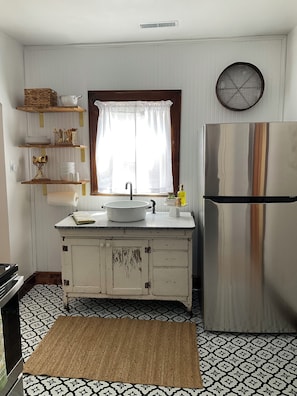 A kitchen with a white sink, a stainless steel refrigerator, and a window with curtains.
