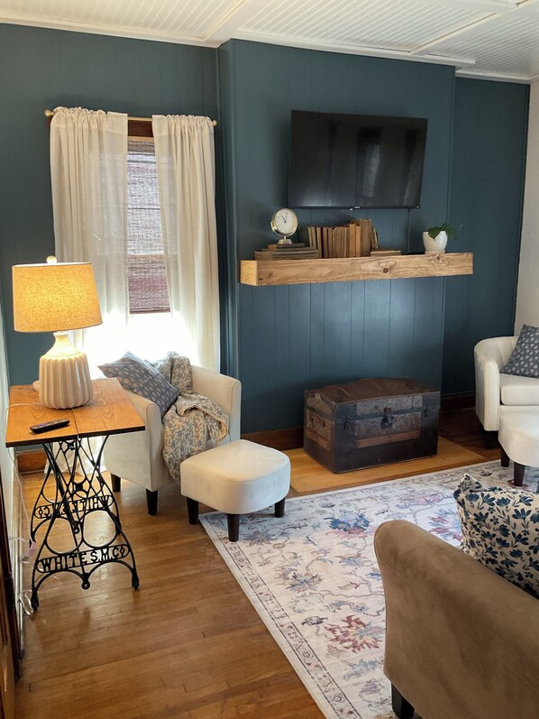 A living room with a sofa, a table with a lamp, a wooden chest, and a mounted television.