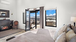 Une chambre d’hôtel dotée d’une cheminée, d’un lit agrémenté de plusieurs oreillers, d’une grande fenêtre offrant une vue dégagée et d’une porte-fenêtre coulissante donnant sur un espace extérieur.