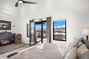 Ein Hotelzimmer mit Kamin, einem Bett mit vielen Kissen, einem großen Fenster mit Blick und einer Schiebetür zu einem Außenbereich.