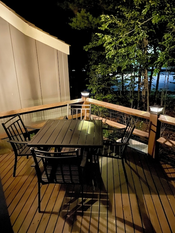 Une terrasse extérieure avec une table et des chaises, entourée d’une rambarde en bois et offrant une vue sur des arbres et une étendue d’eau.
