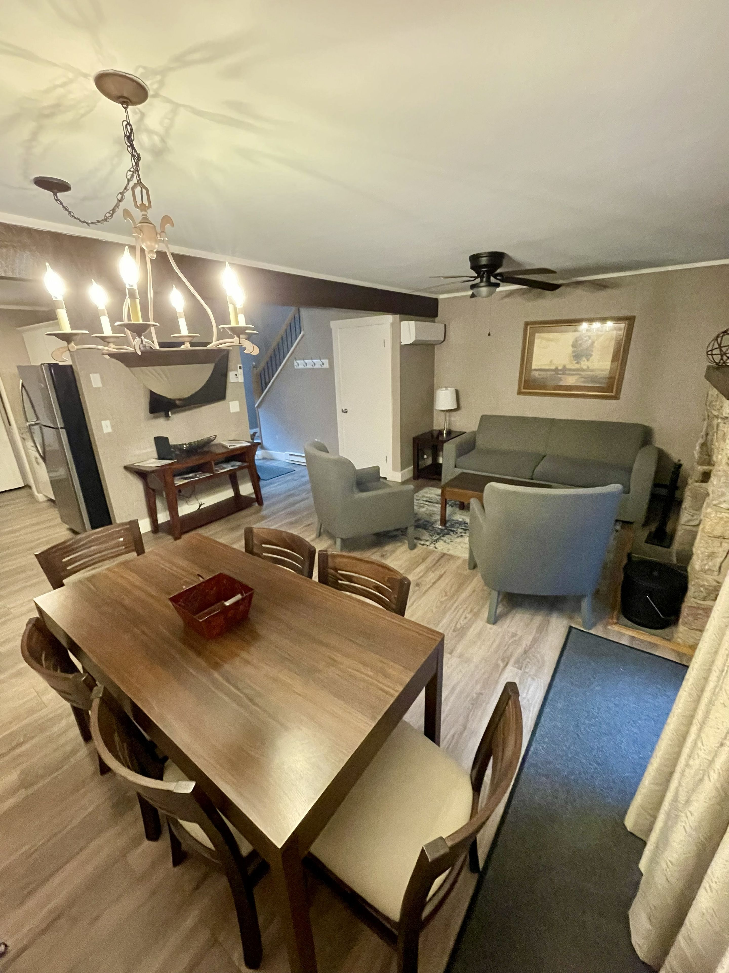Ein Essbereich mit Holztisch und -stühlen, einer Kristallleuchter, einer Couch und einem Deckenventilator.