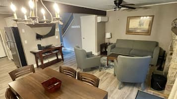 Ein Essbereich mit Holztisch und -stühlen, einer Kristallleuchter, einer Couch und einem Deckenventilator.